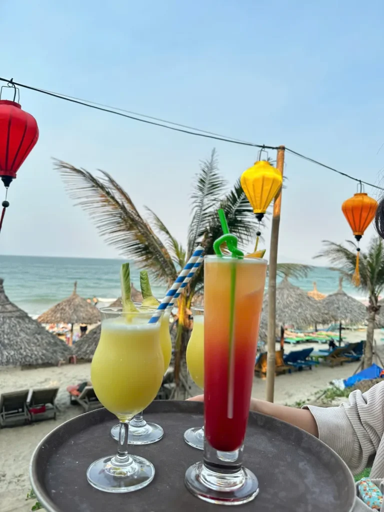 Two cocktails on a tray with An Bang Beach and paper lanterns in the background