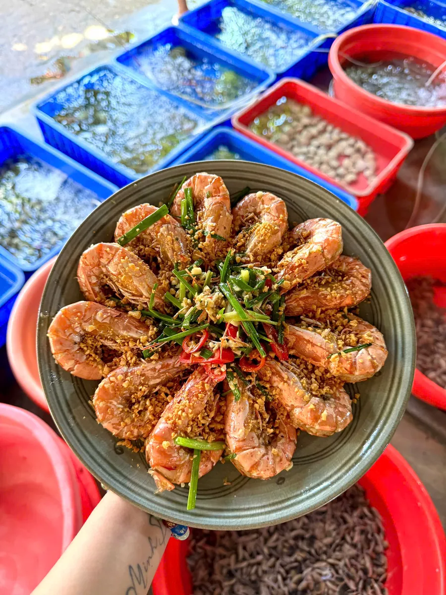 Plate of cooked prawns held above live seafood tanks