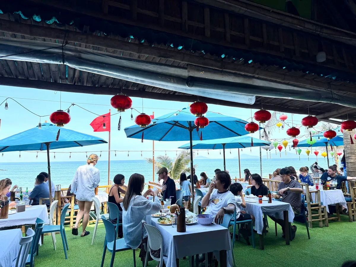 Guests dining under blue umbrellas and red lanterns on Nam Gia's beachfront terrace