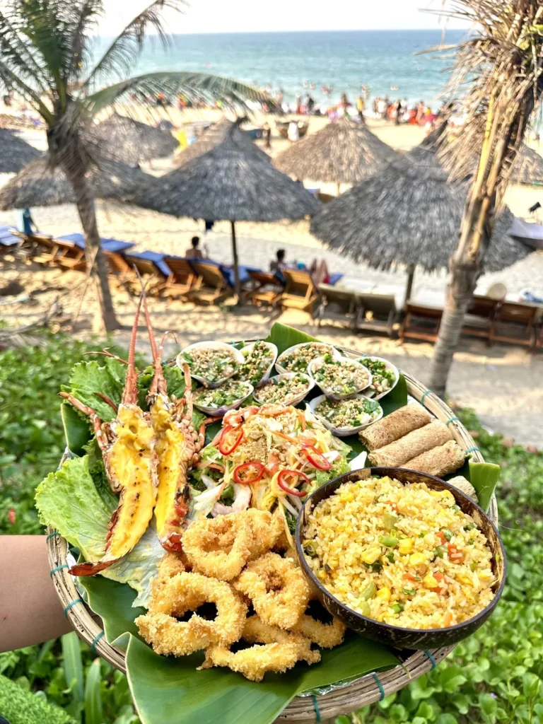 Seafood platter with grilled lobster, fried squid rings, grilled scallops and fried rice, with An Bang Beach behind